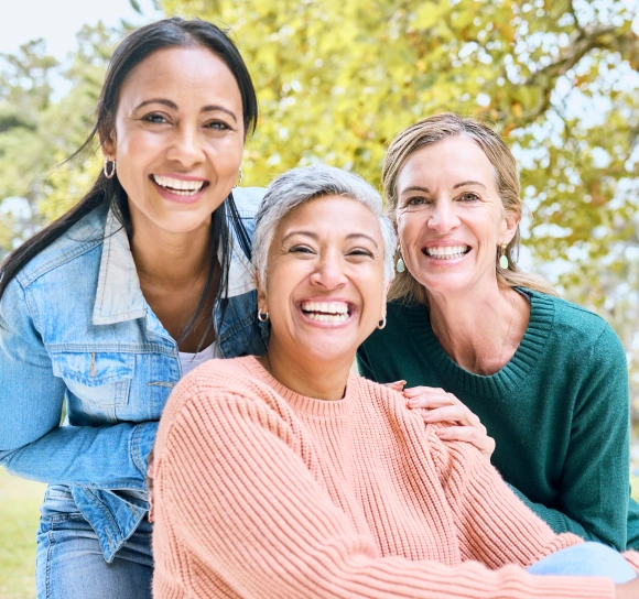 Three smiling women laughing together outdoors, representing the practice's welcoming, community-focused care