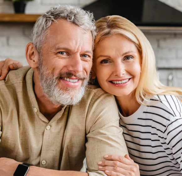Smiling middle-aged couple with healthy teeth, representing dental implants as a permanent solution for missing teeth
