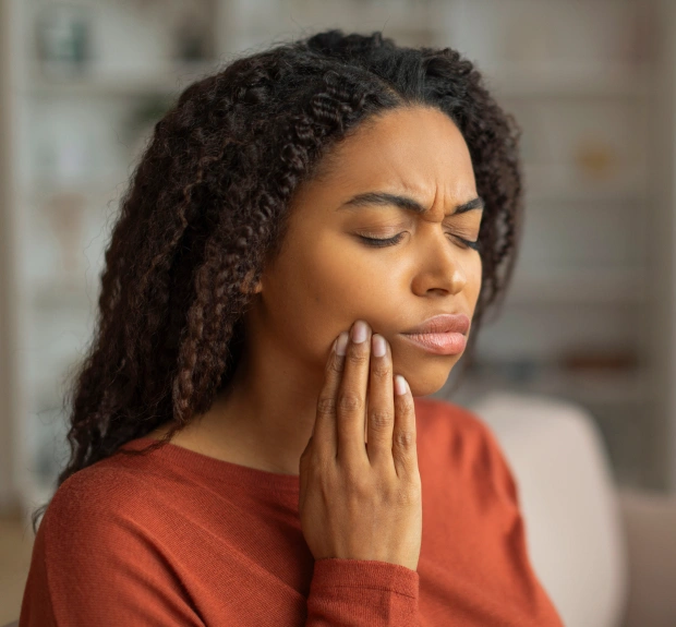 Woman wincing in pain and holding her jaw, representing a dental emergency