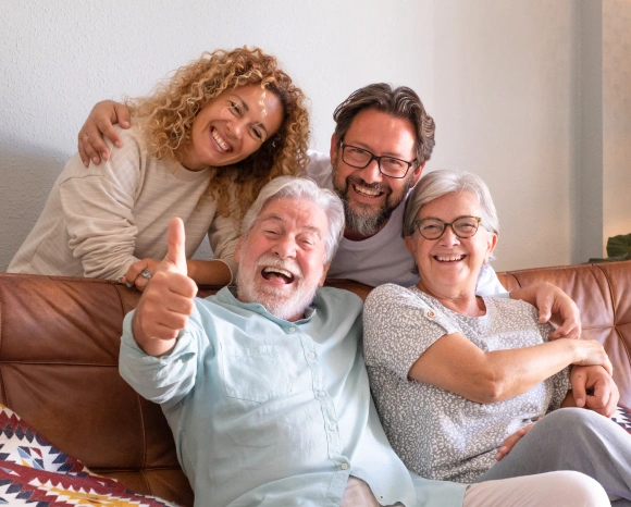 Multi-generational family laughing together on a couch, with grandfather giving a thumbs up, representing patients finding the best dentist