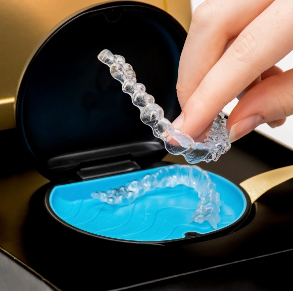 Hand holding a clear Invisalign aligner tray above its storage case