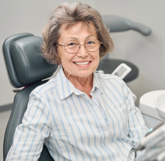 Smiling senior woman with glasses relaxing in a dental chair, representing periodontal therapy patient care