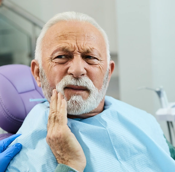 Older male patient in dental chair holding his cheek in pain before a tooth extraction